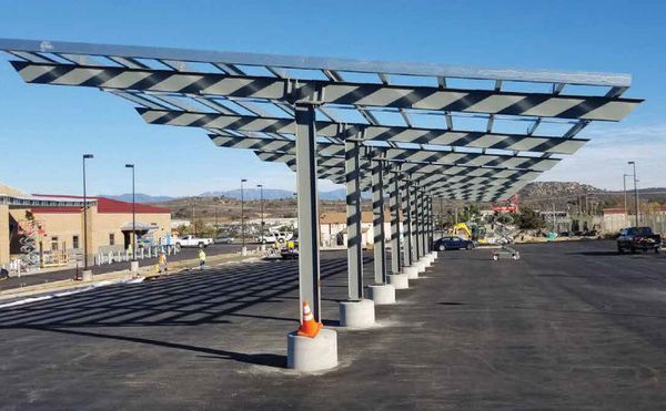 I-beam solar carport installation in parking lot with vehicles and ground-mounted structures